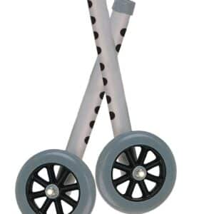 Two gray toy wheels with black spokes, attached to transparent poles with black polka dots, leaning against each other in a crisscross fashion.