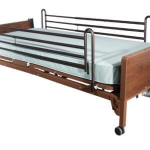 A hospital bed with side rails, a light green mattress, and a wooden headboard and footboard. The bed is on wheels and has a manual crank for adjustments.