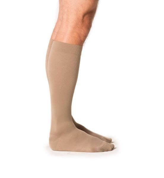 A person wearing knee-high, beige compression socks. The photo is taken from the side, showing the socks covering the lower legs and feet.