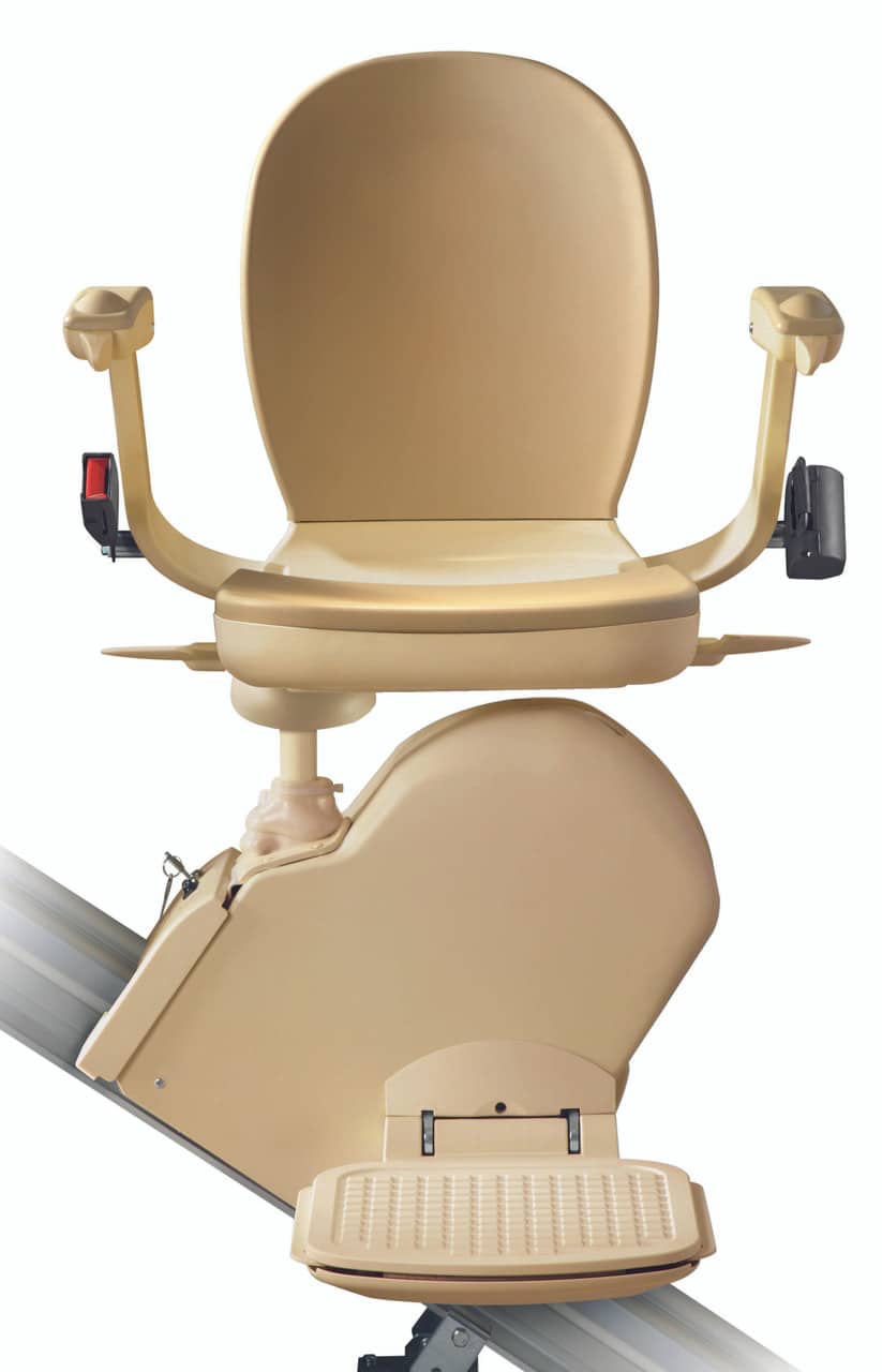 Beige stairlift chair with safety armrests and a foldable footrest, mounted on a track for ascending or descending stairs.