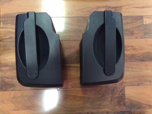 Two black plastic containers with handles sit on a polished wood floor. They are positioned side by side, with their handles facing forward.