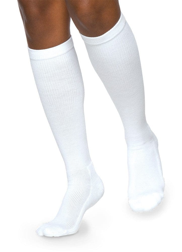 A person wearing knee-high white socks stands on a plain white background, showcasing the ribbed texture and snug fit of the socks.