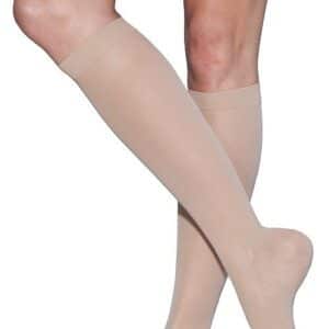 A person wearing knee-high, beige compression stockings with open toes. The image shows the legs from just above the knees down to the feet.