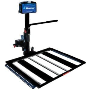 A black and metallic vehicle lift with a platform and vertical support arm. It has a control box labeled Harmar and is designed to attach to a vehicle for transporting mobility devices, such as wheelchairs or scooters.