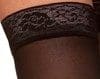 Close-up of a thigh showing a black lace stocking top with a floral pattern. The stocking is sheer and the lace band has intricate detailing. The image focuses on texture and design.