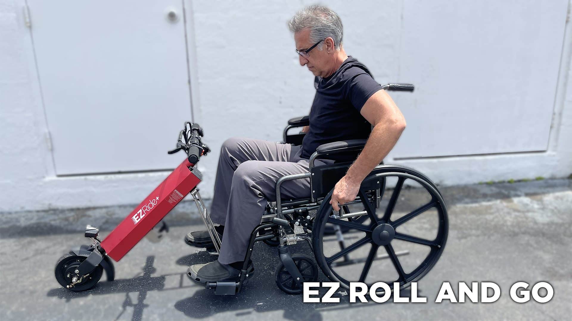 A man in a black shirt and gray pants sits in a wheelchair with a red handlebar attached to the front. The background is a white wall, and the text EZ Roll and Go is displayed in the bottom right corner.