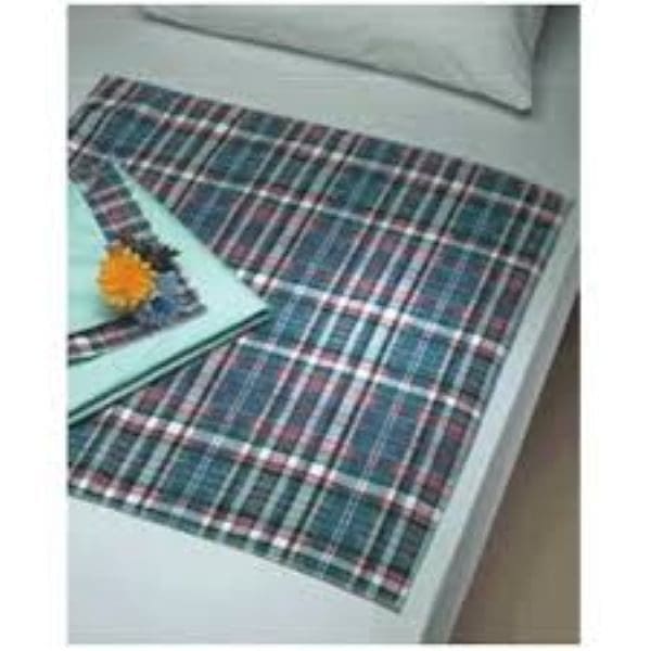 A bed with a green, red, and white plaid blanket placed diagonally. A folded stack of green and blue napkins with a yellow flower on top is on the left side of the bed. A light green pillow is near the back.