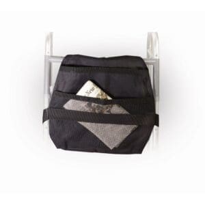 A black storage bag is attached to the back of a walker. The bag has multiple compartments, with a newspaper and a folded piece of fabric visible in the pocket. The walker has a white frame.