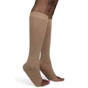 Close-up of a persons legs wearing tan compression socks that cover the calves and feet, with toes peeking out. The socks have a smooth, seamless appearance. The background is plain white.