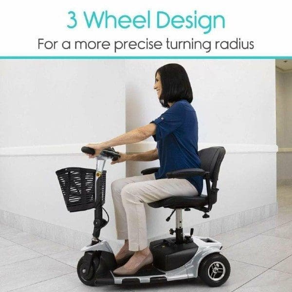 A woman sitting on a three-wheeled mobility scooter indoors. The scooter features a front basket and is designed for a more precise turning radius. The caption at the top reads, 3 Wheel Design - For a more precise turning radius.