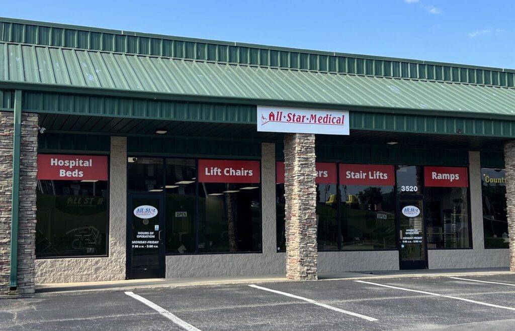 A storefront for All-Star Medical with a green awning and signage advertising hospital beds, lift chairs, stair lifts, and ramps. The exterior features stone columns and large windows with decals displaying contact information.