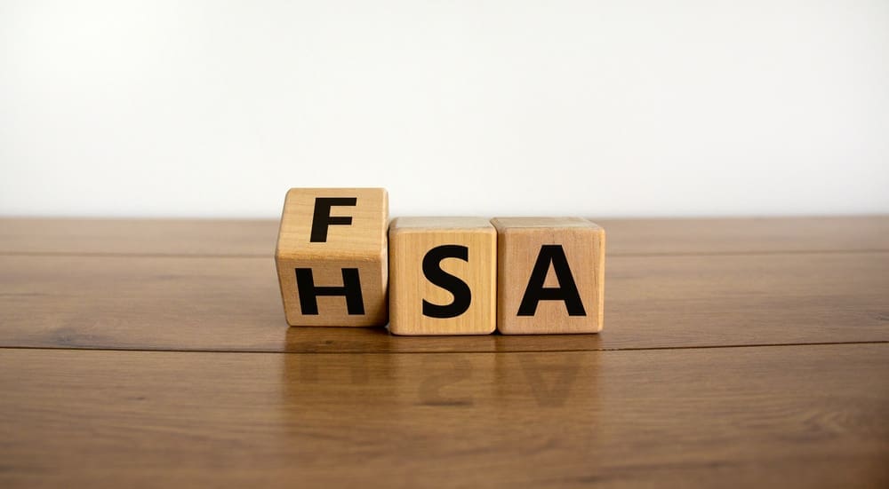 On a wooden surface, three wooden blocks spell out FHSA in bold black letters, against a plain white background. Choosing the right savings account can be confusing; consider your health needs and account flexibility for the best fit.