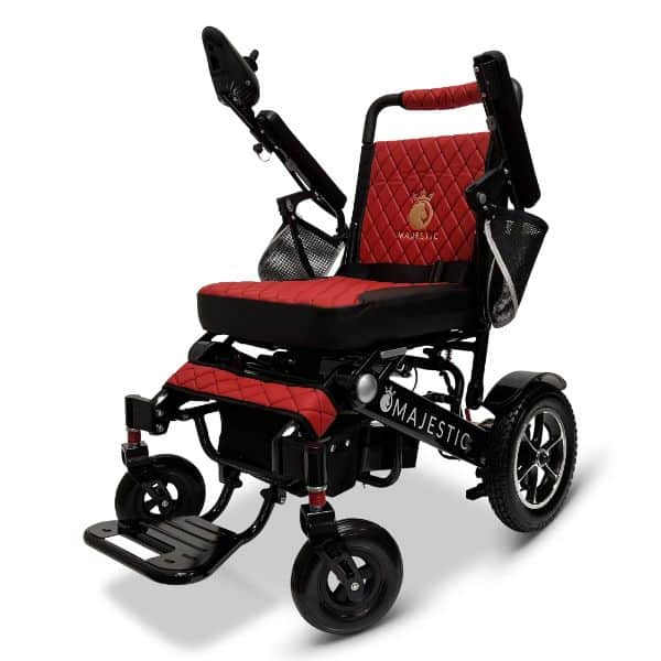 The MAJESTIC IQ-7000 features a sleek black and red design with joystick controls on the armrest, a quilted red padded seat and backrest with logo, large rear wheels, a footrest, and a convenient side storage pouch.