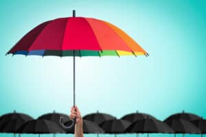 A colorful umbrella stands out among numerous black umbrellas, like demystifying Medicare coverage for durable medical equipment against the complexities of healthcare, all set against a bright turquoise sky.